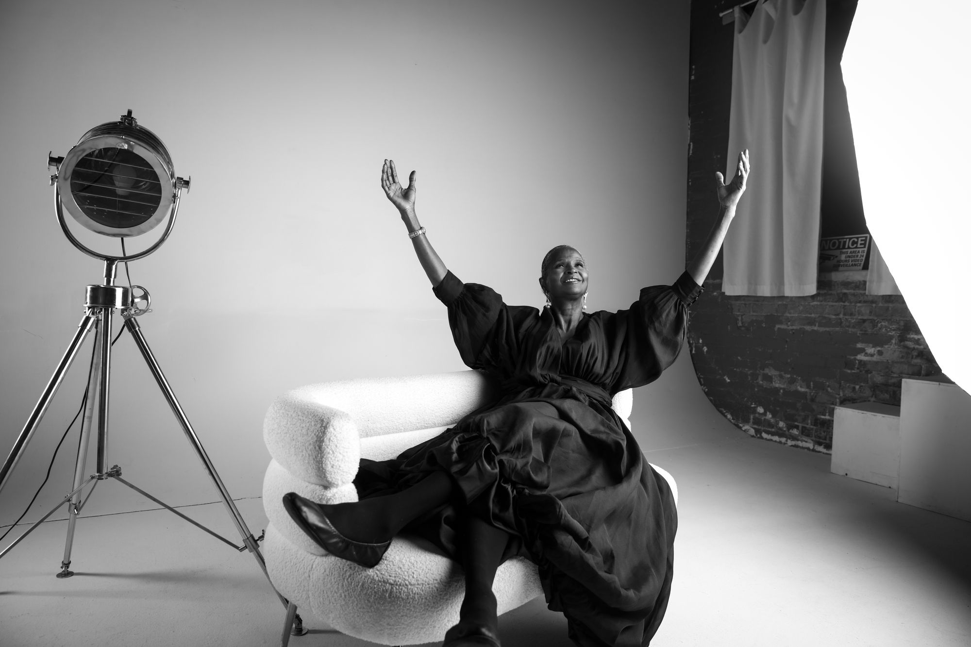 A black and white portrait of a woman raising both hands beside a studio lamp